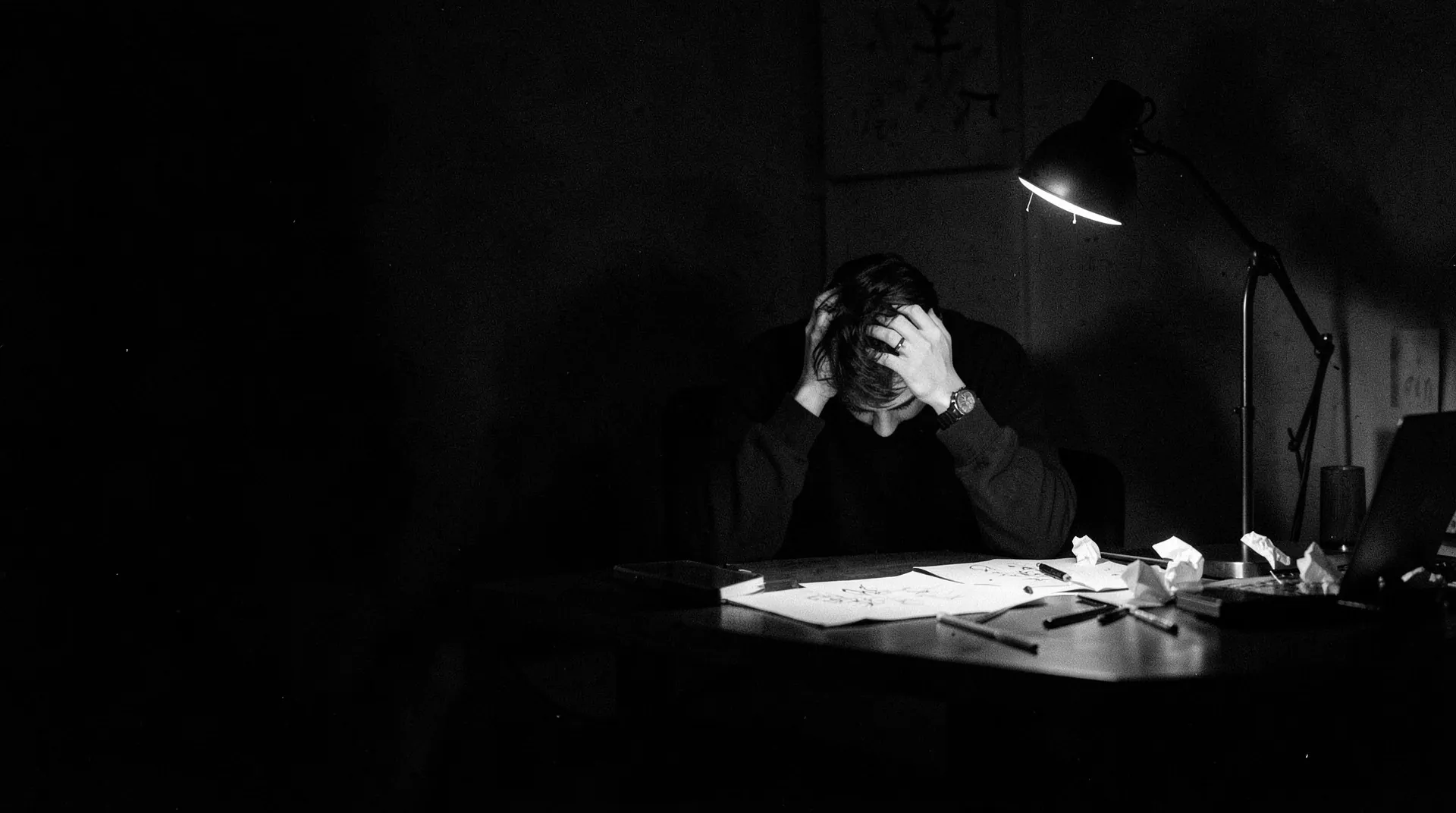 A designer at a cluttered desk late at night, head in hands