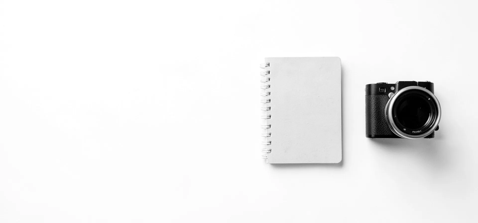 A camera and a notebook on a clean white desk