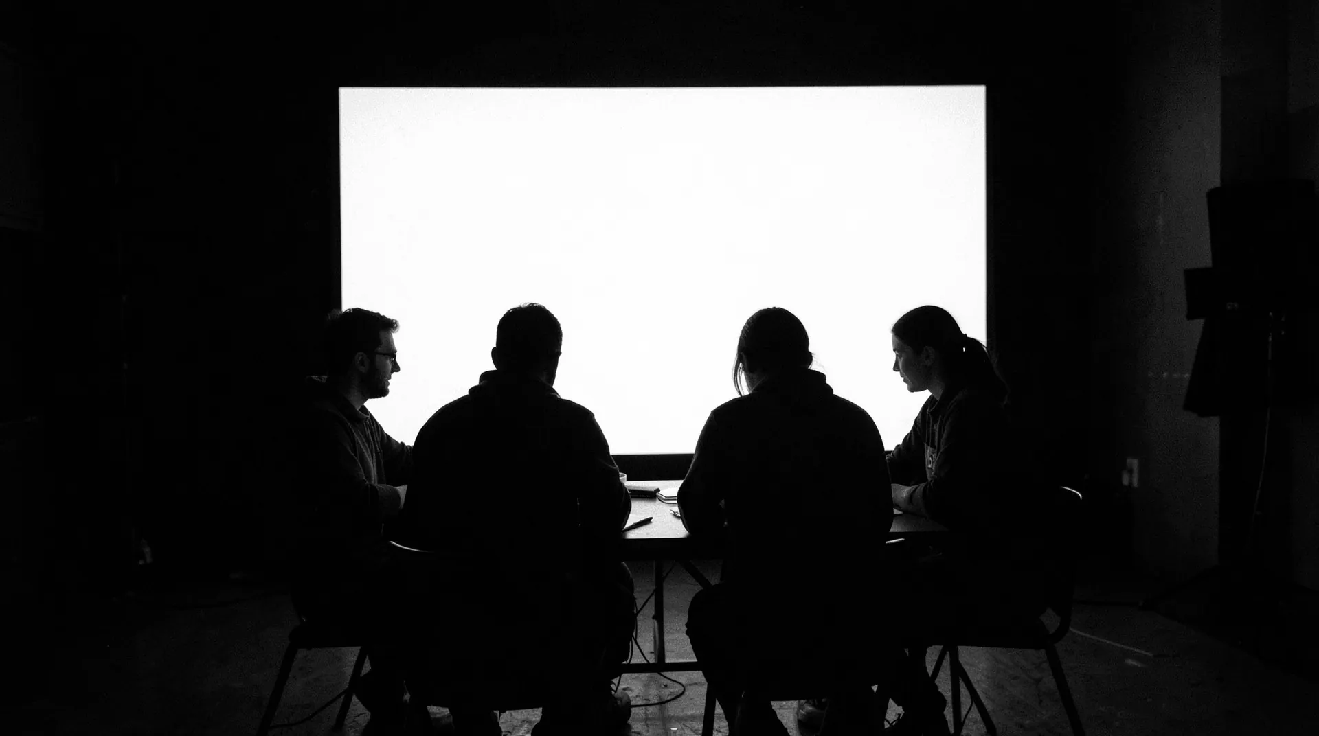 A creative team collaborating around a table in front of a bright screen